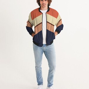 Op de afbeelding: Een marineblauwe bomberjack met een geometrisch patroon in tinten oranje, bruin en beige. De jas heeft een ritssluiting en geribbelde manchetten en tailleband.
