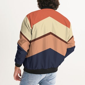 Op de afbeelding: Een bomberjack met een geometrisch patroon in tinten oranje, bruin, beige en donkerblauw.