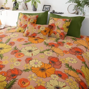 以下が含まれることがあります： ピンクの背景にオレンジ、イエロー、レッドの花柄が描かれた花柄の羽毛布団カバー。羽毛布団カバーは、それに合わせた枕カバーと緑色のアクセント枕を置いたベッドの上に置かれています。