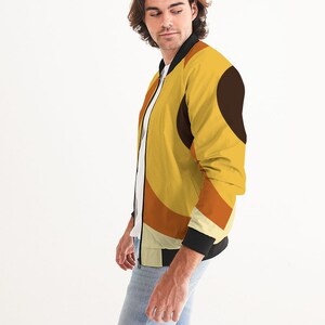 May include: A yellow bomber jacket with a geometric pattern in shades of orange, brown, and white. The jacket has a black zipper and black ribbed cuffs and collar.