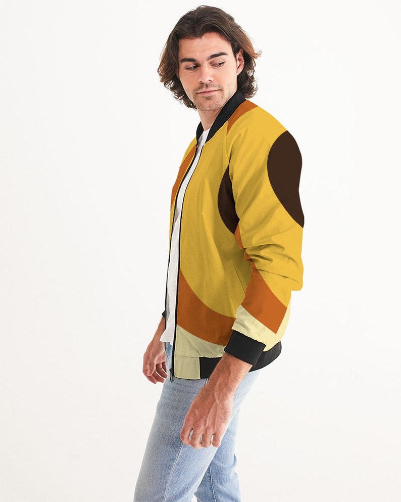 May include: A yellow bomber jacket with a geometric pattern in shades of orange, brown, and white. The jacket has a black zipper and black ribbed cuffs and collar.