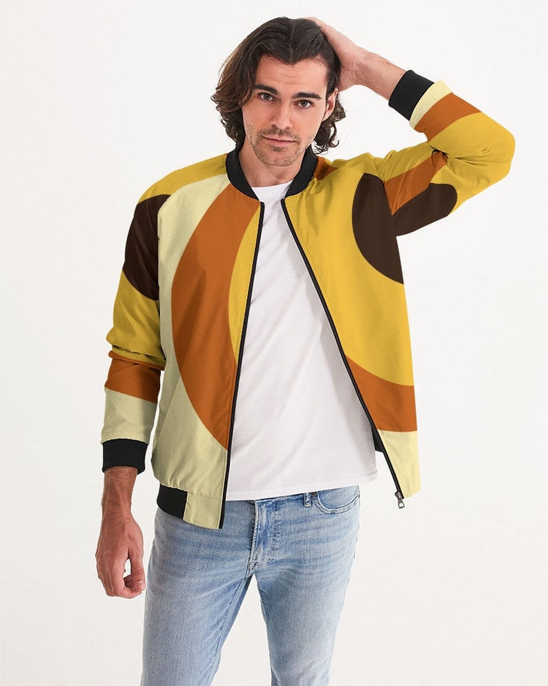 May include: A yellow, orange, and brown bomber jacket with a geometric pattern. The jacket has a black zipper and black ribbed cuffs and waistband.