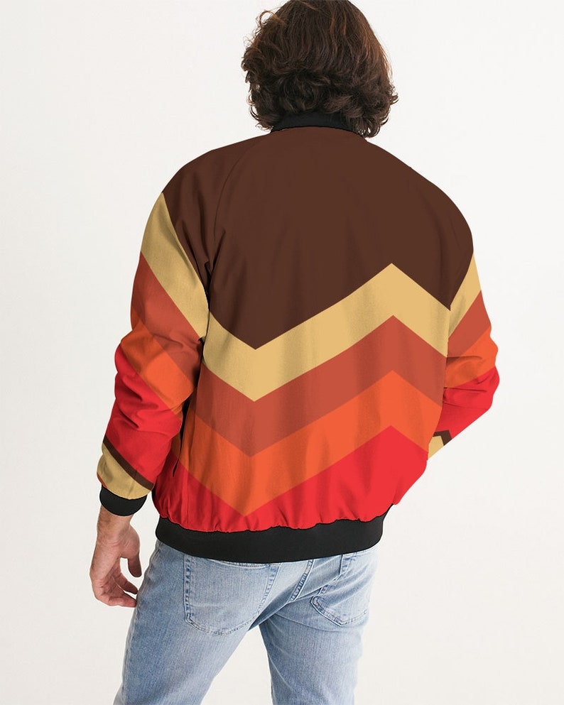 May include: A brown, red, orange, and beige bomber jacket with a chevron pattern. The jacket has a black zipper and a black ribbed collar, cuffs, and waistband.