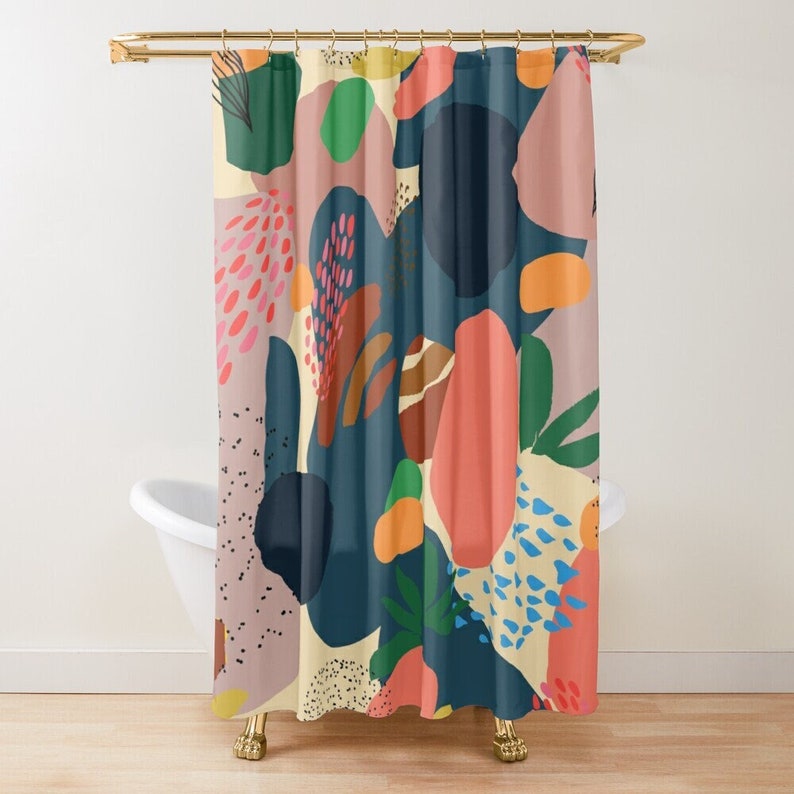 May include: A shower curtain with an abstract design. The pattern features organic shapes in shades of navy, coral, pink, green, and orange against a cream and mauve background. The curtain hangs from a gold-colored rod above a white bathtub.