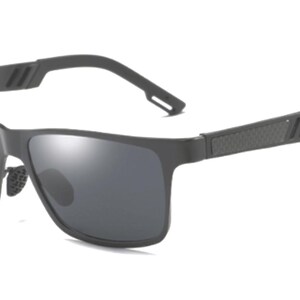 Puede incluir: Gafas de sol rectangulares de color gris oscuro con lentes oscuras. La montura es negra mate, con un patr&oacute;n texturizado y tres l&iacute;neas paralelas en las patillas. El puente nasal tiene un dise&ntilde;o texturizado.