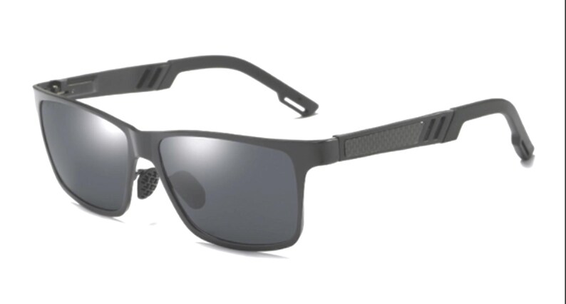 Puede incluir: Gafas de sol rectangulares de color gris oscuro con lentes oscuras. La montura es negra mate, con un patr&oacute;n texturizado y tres l&iacute;neas paralelas en las patillas. El puente nasal tiene un dise&ntilde;o texturizado.