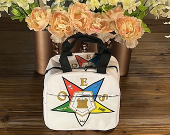 May include: White lunch bag with a black handle and a colorful emblem. The emblem features a star with the letter "E" in the center, surrounded by other symbols and letters. The bag is sitting on a wooden surface.