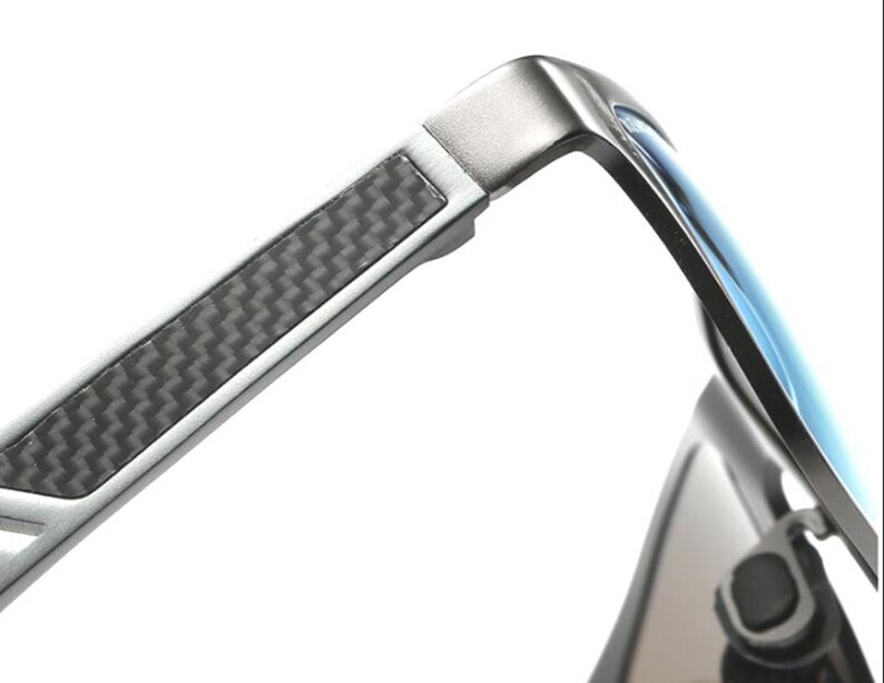 Puede incluir: Primer plano de gafas de sol modernas con montura de metal plateado y lentes azules. Las patillas presentan un patr&oacute;n de fibra de carbono para un look elegante. Dise&ntilde;o elegante y contempor&aacute;neo.