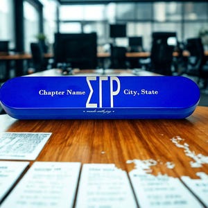 May include: A royal blue, elongated, oval-shaped desk sign featuring the Greek letters ΣΓΡ in white, flanked by the text Chapter Name and City, State, with the phrase made with joy printed in a smaller white script font along the bottom edge.