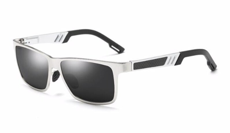 Puede incluir: Gafas de sol plateadas con lentes oscuras. Las gafas tienen forma rectangular con detalles negros en las patillas y las varillas. Las lentes son oscuras y la montura es de color plateado brillante.