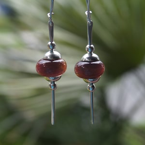 May include: A pair of silver dangle earrings with a dark red glass bead on each earring.