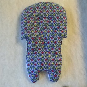 Può includere: Un cuscino per seggiolino per bambini blu con un motivo colorato di cerchi e quadrati. Il cuscino è imbottito e ha un poggiatesta.