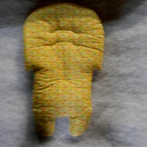 Può includere: Un inserto giallo imbottito per seggiolino auto per bambini con un motivo a pois colorati. L'inserto ha un poggiatesta e una sezione del corpo con due aperture per le gambe. Il tessuto è morbido e trapuntato.