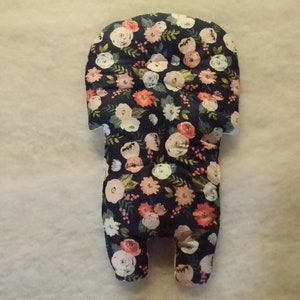 May include: A floral patterned baby car seat insert. The insert features a dark navy blue background with a repeating pattern of pink, white, and peach-colored flowers and green leaves. The insert is designed to provide comfort and support for infants.