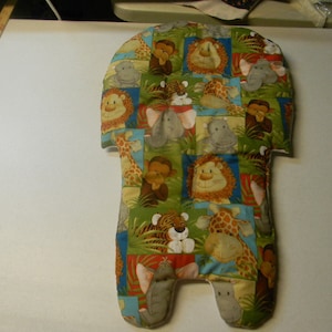 Può includere: Inserto imbottito per seggiolino auto per bambini con un design patchwork che presenta vari animali della giungla, tra cui leoni, scimmie, elefanti, giraffe e tigri. Il tessuto è un mix di quadrati verdi, blu e rossi, creando un motivo giocoso e colorato.