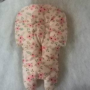 Può includere: Inserto imbottito per seggiolino auto per bambini con motivo floreale. L'inserto è principalmente beige con un motivo ripetuto di fiori rosa e foglie verdi. Ha una parte superiore arrotondata e due aperture per le gambe nella parte inferiore.