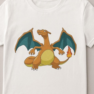 Puede incluir: Camiseta blanca con una ilustración de dibujos animados de Charizard, un Pokémon de tipo fuego y volador. El diseño muestra a Charizard en colores naranja, amarillo y verde azulado. La camiseta está hecha de un material suave y cómodo.