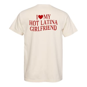 May include: Cream-colored t-shirt with the text "I ❤️ MY HOT LATINA GIRLFRIEND" in red. The design includes a red heart symbol above the word "MY". The shirt has short sleeves and a crew neck.