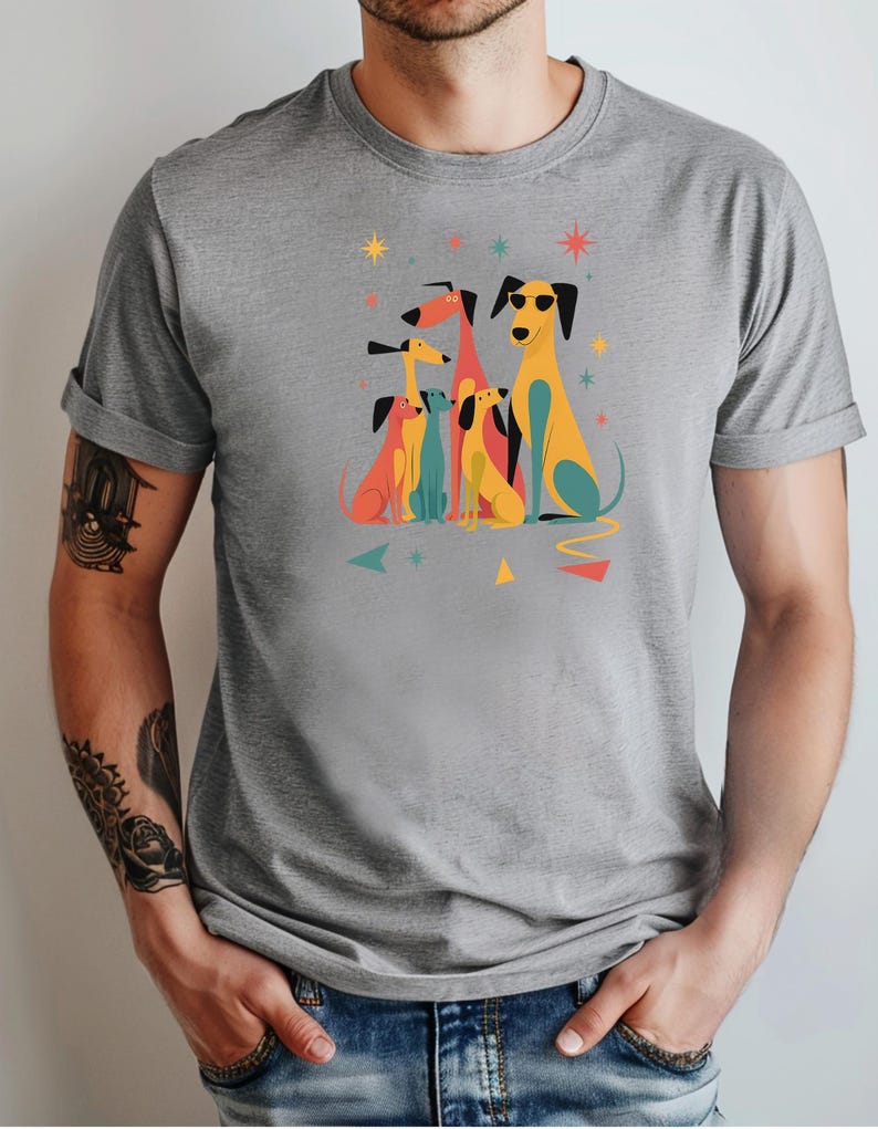 Op de afbeelding: Grijs t-shirt met een kleurrijke afbeelding van gestileerde honden. De honden zijn afgebeeld in verschillende kleuren, waaronder geel, rood en blauw, sommige dragen een zonnebril. Geometrische vormen en sterren omringen de honden.