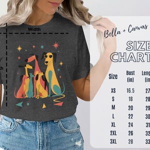 Op de afbeelding: Donkergrijs Bella + Canvas 3001 T-shirt met een kleurrijke illustratie van cartoonhonden met een zonnebril. Het shirt bevat een maattabel met borst- en lengtematen in cm.