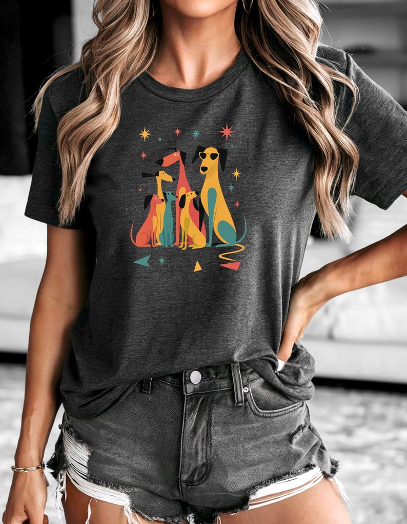 Op de afbeelding: Donkergrijs t-shirt met een kleurrijke afbeelding van gestileerde honden. De honden zijn in verschillende kleuren, waaronder geel, blauw en rood, sommige dragen een zonnebril. Geometrische vormen en sterren omringen de honden.