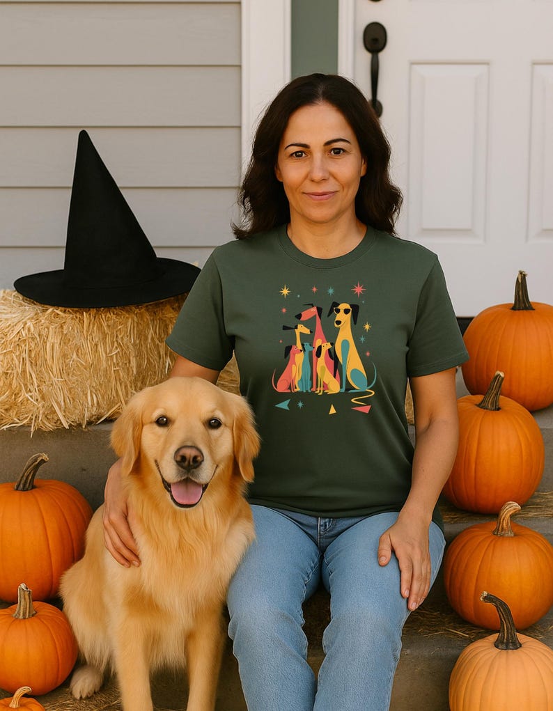 Op de afbeelding: Een vrouw draagt een groen t-shirt met een kleurrijke hondenafbeelding, zittend met een golden retriever en pompoenen. Een zwarte heksenhoed ligt op een hooibaal. De sc&egrave;ne heeft een herfst- of Halloween-thema.