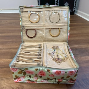 May include: Open jewelry travel case with a floral rose pattern in pink and green. The case is filled with gold bangles, necklaces, and small zippered pouches. The interior is beige.