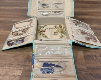 May include: A light blue floral jewelry organizer case with multiple fold-out compartments, clear zippered pockets, and beige interior lining. The organizer is filled with various necklaces, earrings, and bracelets, showcasing organized storage for accessories.