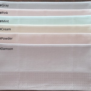 May include: Six waffle weave kitchen towels in different colors, stacked on top of each other. The colors are gray, pink, mint, cream, powder, and damson. Each towel has a label with a color name and a hashtag.