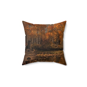 May include: A square throw pillow featuring a printed autumn forest scene with orange and brown trees reflected in a dark pond. A wooden signpost in the foreground displays the text Happy Halloween with a small pumpkin icon centered below it.