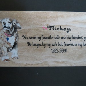 May include: A beige stone memorial with a painted image of a brown and white dog. The inscription reads "Mickey, You were my favorite hello and my hardest goodbye. No longer by my side but forever in my heart. 1992-2006."