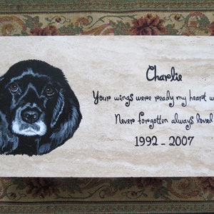 May include: A black and white painted portrait of a dog on a beige stone plaque. The plaque reads "Charlie, Your wings were ready my heart was not. Never forgotten always loved. 1992 - 2007."
