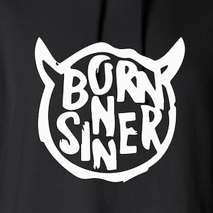 Könnte beinhalten: Schwarzer Hoodie mit einem weißen Grafikdruck eines Kreises mit den Worten "Born Sinner" darin und zwei Teufelshörnern oben.