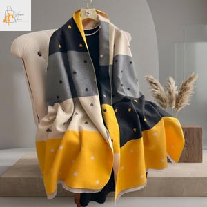 Może przedstawiać: Prostokątny szalik z wzorem bloków kolorów w kolorze czarnym, szarym, kremowym i żółtym. Szalik posiada małe wzory serc w kolorze białym i złotym. Szalik jest narzucony na krzesło, prezentując swój design i fakturę.