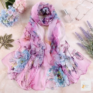 May include: A lightweight, semi-sheer rectangular scarf featuring a vibrant watercolor-style floral print in shades of pink, purple, and blue. The fabric displays a repeating pattern of large, abstract blossoms and foliage across the entire surface.