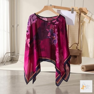 Könnte beinhalten: Ein transparentes, magentafarbenes Oberteil mit einem Blumenmuster in Rosa- und Lilatönen. Das Oberteil hat einen schwarzen Ausschnitt und einen marineblauen und goldenen Rand. Das Kleidungsstück hängt an einem Holzbügel.