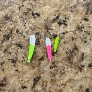 May include: Three colorful fishing lures with silver hooks. The lures are painted in white, neon green, and pink. The lures are designed to attract fish and are used in freshwater fishing.
