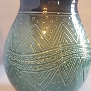 May include: A ceramic vase with a teal glaze and a geometric pattern. The vase has a wide mouth and a rounded body.