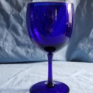 May include: A cobalt blue glass wine goblet with a wide bowl and a tall stem. The goblet is sitting on a blue fabric surface.