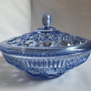 May include: A vintage blue glass candy dish with a lid. The dish has a textured, patterned design on the lid and the bowl. The lid has a small, rounded handle. The bowl has a ribbed design around the base.