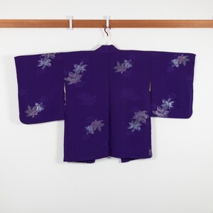 Könnte beinhalten: Ein lilafarbener Kimono mit Blumenmuster. Der Kimono hängt an einem Holzbügel.