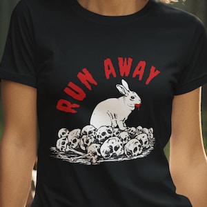 Op de afbeelding: Een zwart T-shirt met een witte konijn afbeelding en de tekst "RUN AWAY" in rood. Het konijn zit op een stapel schedels.