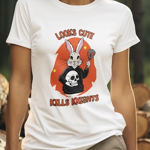 Könnte beinhalten: Weißes T-Shirt mit einem Grafikdesign eines Kaninchens in einem schwarzen Kapuzenpullover, das einen Totenkopf hält. Der Text "LOOKS CUTE KILLS KNIGHTS" ist aufgedruckt. Der Hintergrund ist ein Wald.