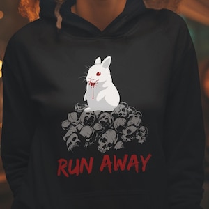 Puede incluir: Sudadera negra con un conejo blanco con ojos rojos y sangre goteando de su boca, sentado sobre una pila de cráneos. El texto "RUN AWAY" está impreso debajo del conejo.