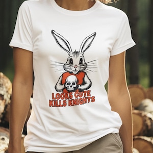 Könnte beinhalten: Weißes T-Shirt mit einem Cartoon-Kaninchen, das einen Totenkopf hält, mit dem Text "LOOKS CUTE KILLS KNIGHTS" in Rot. Die Person trägt eine khakifarbene Hose in einer Waldumgebung.