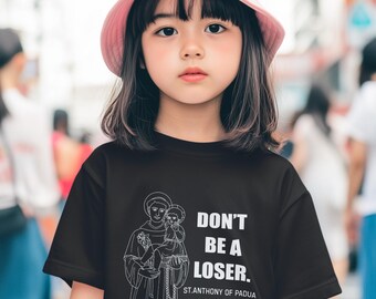 May include: A young person wearing a black t-shirt with the text "DON'T BE A LOSER." and an illustration of a saint holding a child. The shirt also includes the text "ST. ANTHONY OF PADUA." The person is wearing a pink bucket hat.