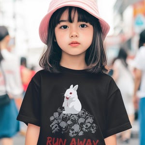 May include: A young person wearing a black t-shirt with a graphic of a white rabbit covered in blood, sitting on a pile of skulls. The text "RUN AWAY" is printed in red. The person is also wearing a pink bucket hat.