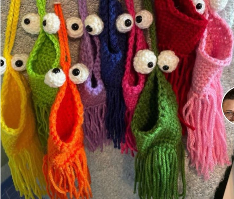 Puede incluir: Una colecci&oacute;n de bolsas colgantes de ganchillo con flecos coloridos y ojos saltones. Las bolsas son de varios colores, incluyendo verde, naranja, amarillo, rosa, morado y rojo.
