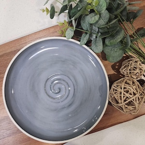 May include: A large, grey ceramic serving dish with a white rim and a spiral design in the centre.