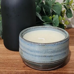 May include: A blue and white ceramic candle holder with a white candle inside. The candle holder has a striped pattern and is sitting on a wooden surface.
